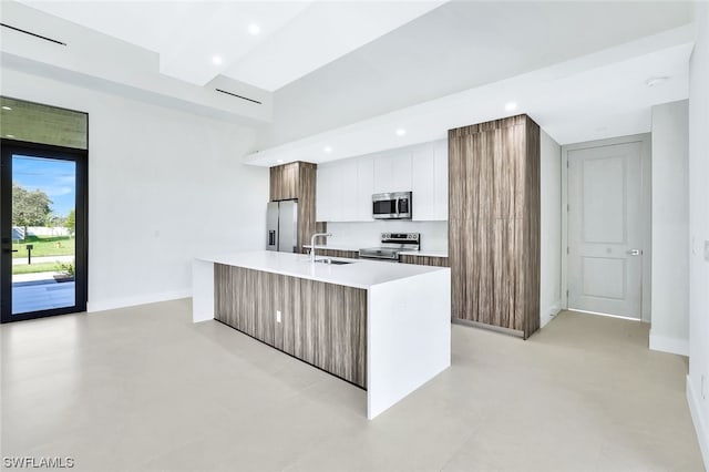 kitchen with an island with sink, light tile floors, white cabinets, stainless steel appliances, and tasteful backsplash