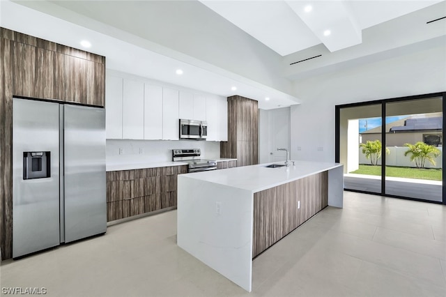 kitchen with an island with sink, stainless steel appliances, light tile floors, white cabinets, and sink