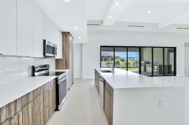 kitchen with sink, stainless steel appliances, a center island with sink, white cabinets, and beam ceiling