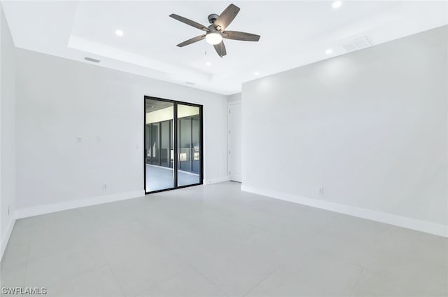 empty room with light tile flooring, ceiling fan, and a tray ceiling