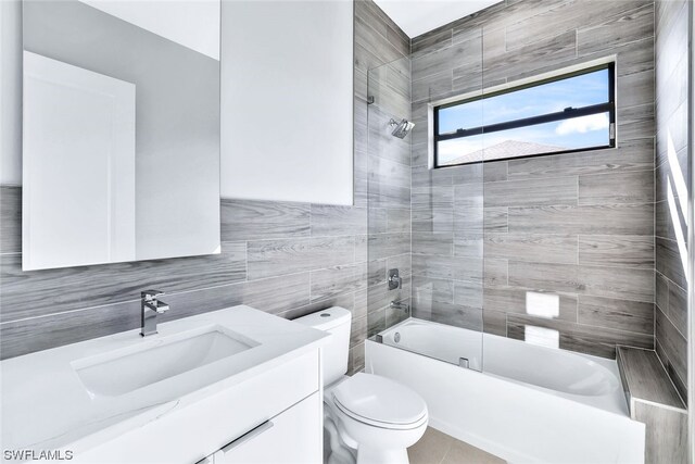 full bathroom featuring tile walls, tile floors, tiled shower / bath, vanity with extensive cabinet space, and toilet