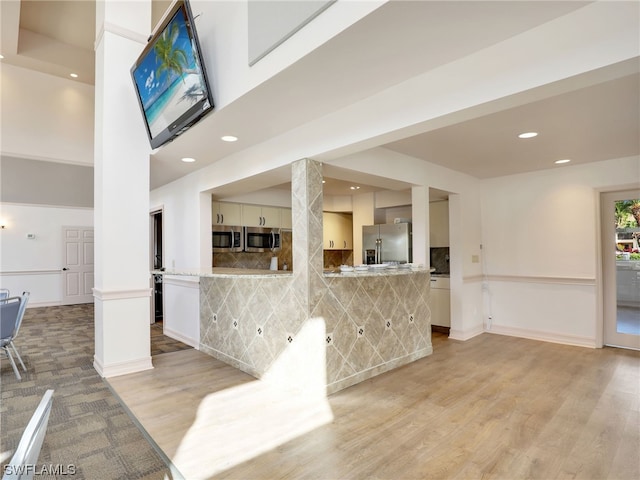 interior space featuring a high ceiling, appliances with stainless steel finishes, light wood-type flooring, and kitchen peninsula