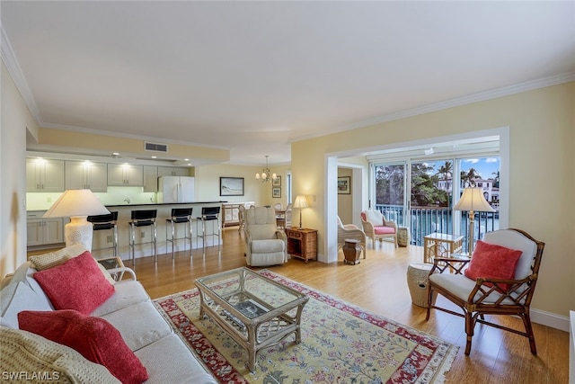 living room featuring crown molding, an inviting chandelier, and light hardwood / wood-style flooring