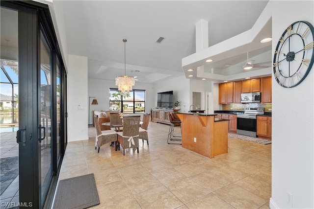 kitchen with an island with sink, stainless steel appliances, decorative light fixtures, a kitchen bar, and a raised ceiling