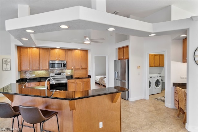 kitchen featuring ceiling fan, a kitchen breakfast bar, stainless steel appliances, tasteful backsplash, and washing machine and dryer