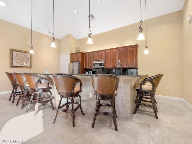 kitchen featuring decorative light fixtures, appliances with stainless steel finishes, kitchen peninsula, and a breakfast bar