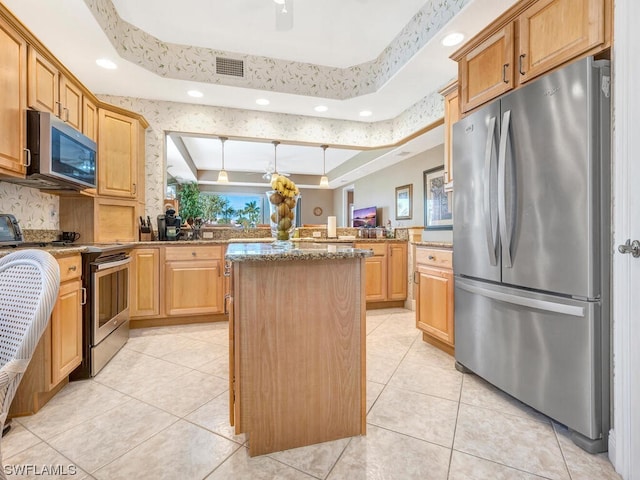 kitchen featuring appliances with stainless steel finishes, stone countertops, light tile patterned floors, a tray ceiling, and a center island