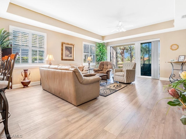 living room featuring a healthy amount of sunlight, ceiling fan, light hardwood / wood-style flooring, and a raised ceiling