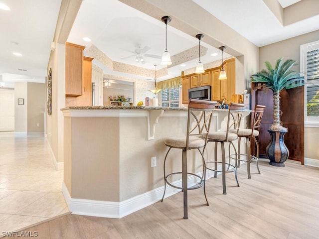 kitchen featuring pendant lighting, light wood-type flooring, a tray ceiling, and kitchen peninsula