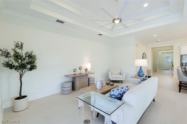 living room with a raised ceiling, ceiling fan, and ornamental molding