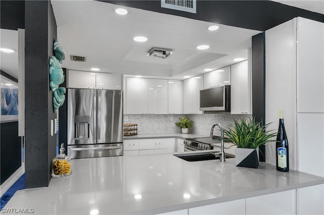 kitchen with a raised ceiling, kitchen peninsula, stainless steel fridge, white cabinets, and sink