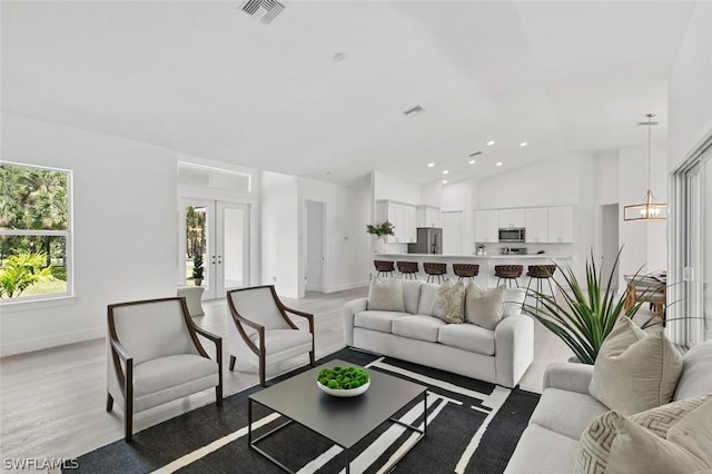 living area featuring lofted ceiling, visible vents, baseboards, light wood-style floors, and french doors