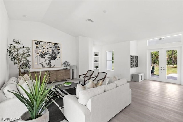 living room with wood finished floors, visible vents, built in features, vaulted ceiling, and french doors