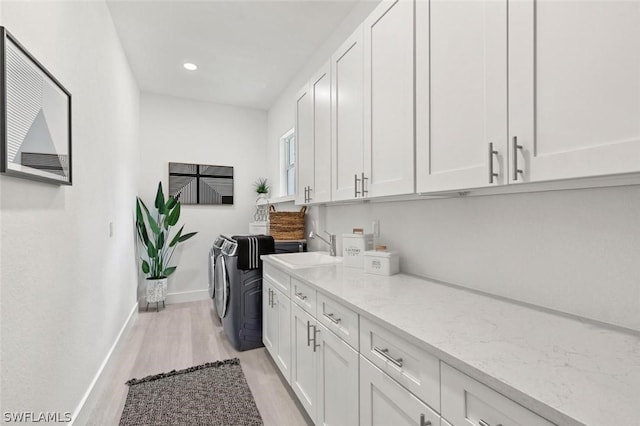 washroom featuring a sink, baseboards, cabinet space, light wood finished floors, and washing machine and clothes dryer