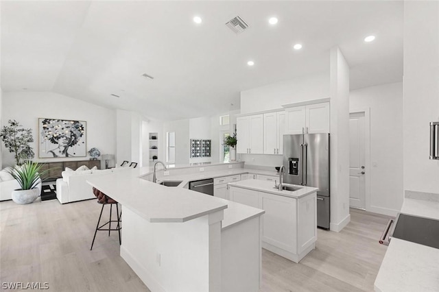 kitchen with visible vents, an island with sink, stainless steel appliances, light wood-style floors, and a sink