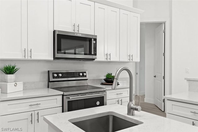 kitchen featuring light stone counters, stainless steel appliances, white cabinetry, a sink, and wood finished floors