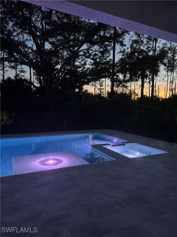 pool at dusk with an in ground hot tub