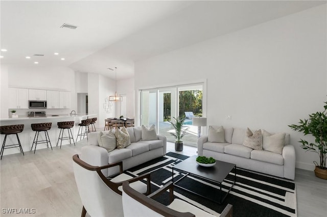 living room with recessed lighting, visible vents, high vaulted ceiling, light wood-type flooring, and baseboards