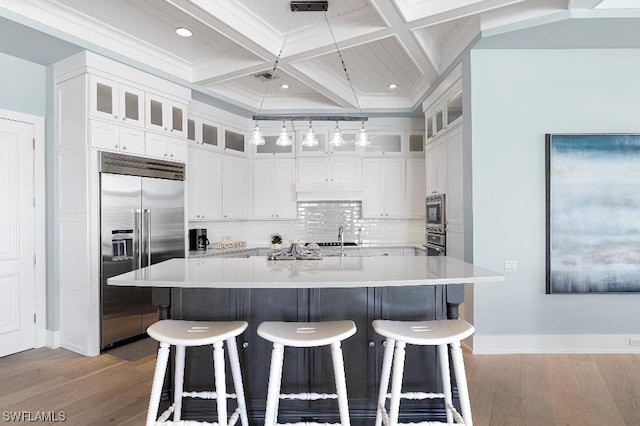 kitchen with built in refrigerator, a kitchen island with sink, pendant lighting, white cabinets, and coffered ceiling