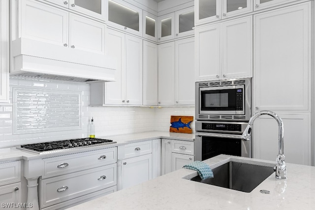 kitchen featuring backsplash, stainless steel appliances, white cabinetry, and light stone counters