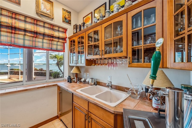 kitchen with light tile flooring, a water view, tile countertops, and sink