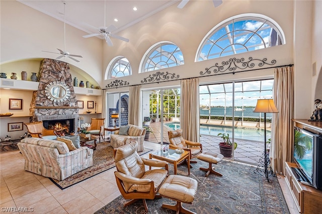 living room with a high ceiling, ceiling fan, light tile floors, and a stone fireplace