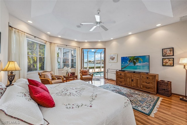 bedroom with ceiling fan, a water view, light hardwood / wood-style flooring, access to outside, and a raised ceiling