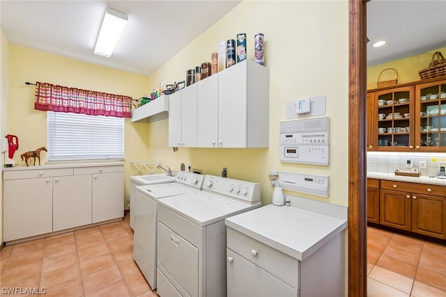 clothes washing area featuring washer and clothes dryer, cabinets, sink, and light tile flooring