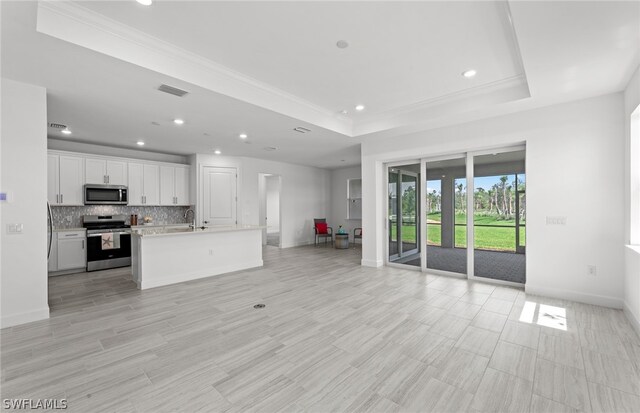 kitchen with backsplash, a center island with sink, a tray ceiling, white cabinetry, and appliances with stainless steel finishes