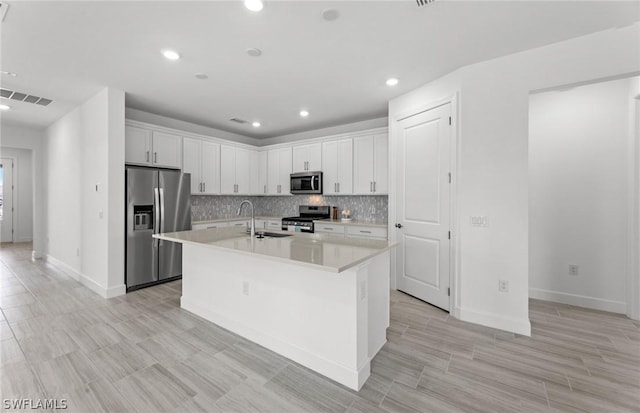 kitchen featuring sink, white cabinetry, stainless steel appliances, tasteful backsplash, and a center island with sink