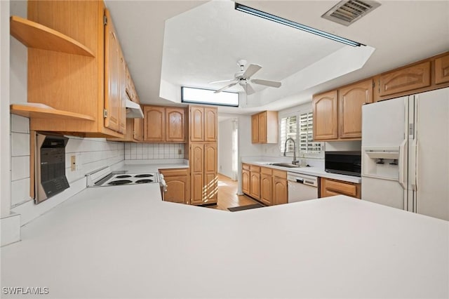 kitchen featuring sink, white appliances, ceiling fan, backsplash, and a tray ceiling