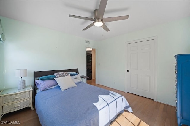 bedroom featuring stacked washer and dryer, hardwood / wood-style flooring, and ceiling fan