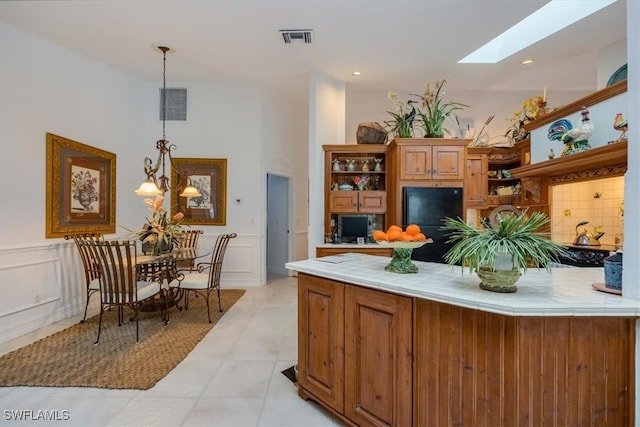 kitchen with a skylight, backsplash, a chandelier, decorative light fixtures, and light tile patterned flooring