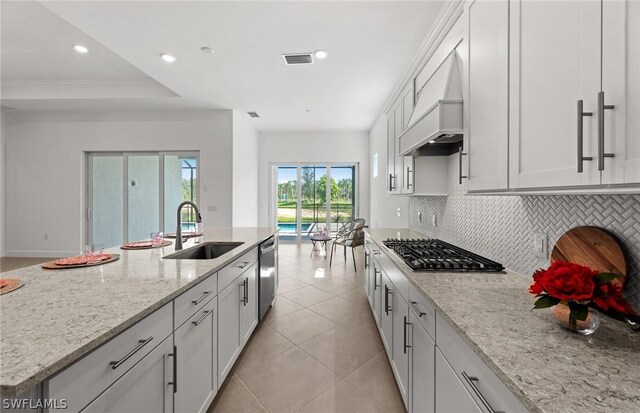 kitchen with light stone countertops, appliances with stainless steel finishes, tasteful backsplash, custom range hood, and sink