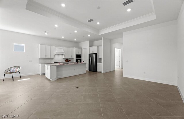 kitchen featuring premium range hood, a kitchen island with sink, a tray ceiling, and stainless steel appliances