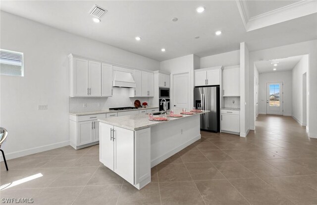 kitchen featuring white cabinets, premium range hood, an island with sink, and appliances with stainless steel finishes