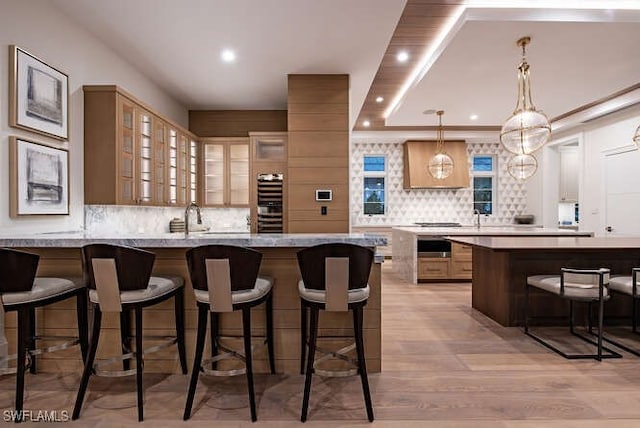 bar with backsplash, sink, hanging light fixtures, light hardwood / wood-style flooring, and light stone countertops