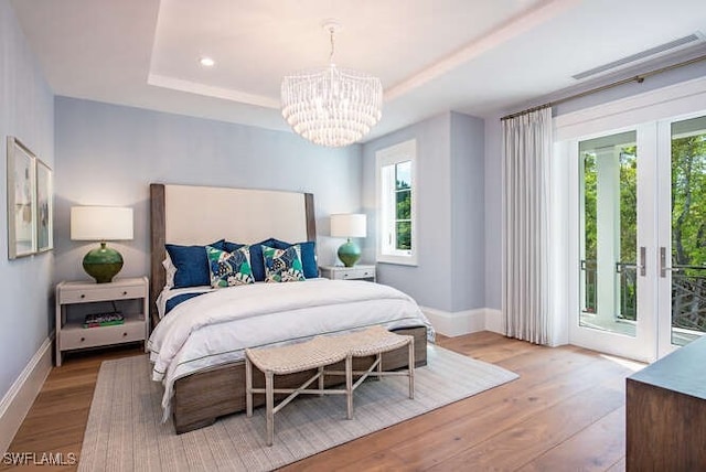 bedroom featuring a notable chandelier, light hardwood / wood-style floors, a raised ceiling, and access to outside