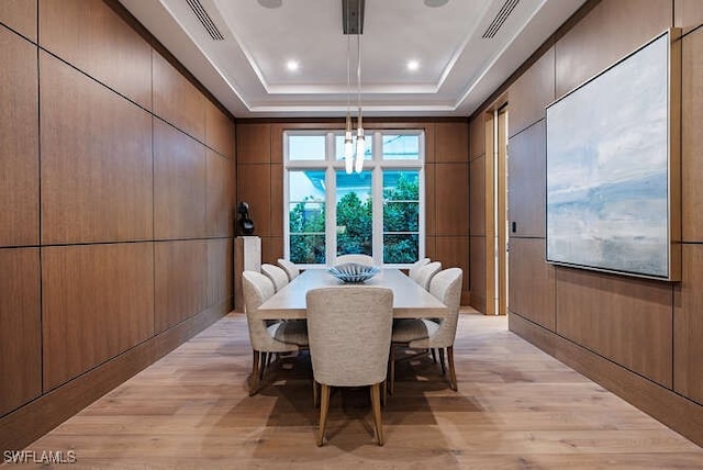 dining area with wood walls, light wood-type flooring, and a tray ceiling