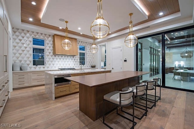 kitchen with backsplash, a raised ceiling, light hardwood / wood-style flooring, a kitchen island, and hanging light fixtures