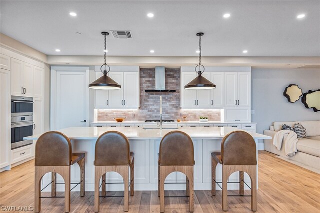 kitchen featuring wall chimney range hood, pendant lighting, and white cabinetry