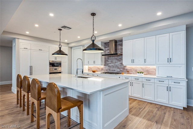 kitchen featuring wall chimney range hood, light hardwood / wood-style floors, an island with sink, and a breakfast bar