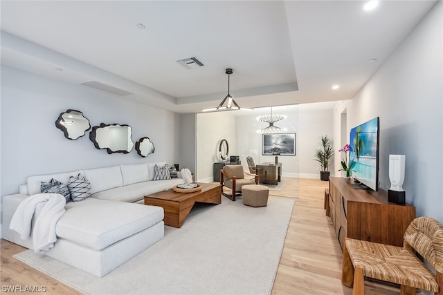 living room featuring a raised ceiling, an inviting chandelier, and light hardwood / wood-style flooring