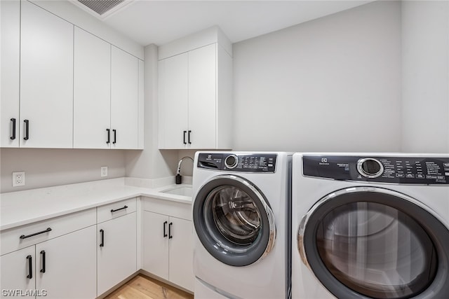 laundry area featuring separate washer and dryer, light hardwood / wood-style floors, cabinets, and sink