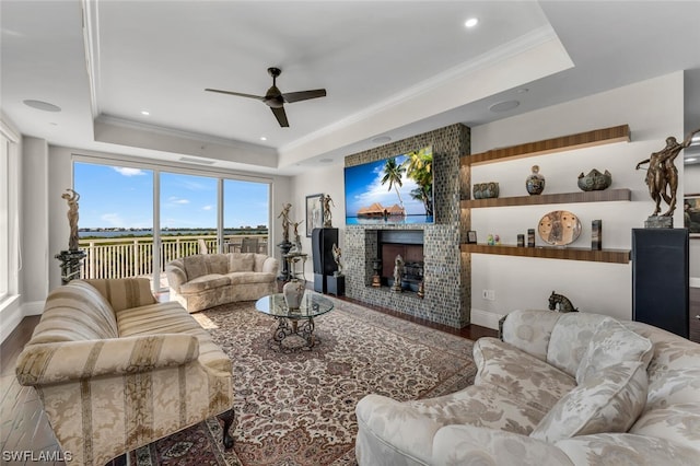 living room with ceiling fan, wood-type flooring, crown molding, and a tray ceiling