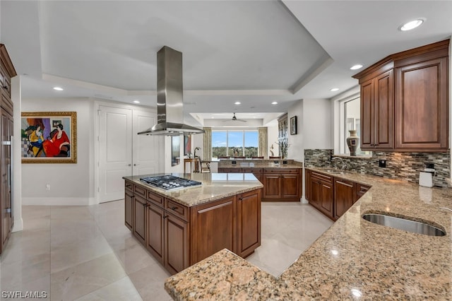 kitchen featuring light stone countertops, backsplash, island exhaust hood, kitchen peninsula, and stainless steel gas stovetop