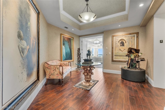 sitting room with dark hardwood / wood-style flooring, a raised ceiling, and crown molding