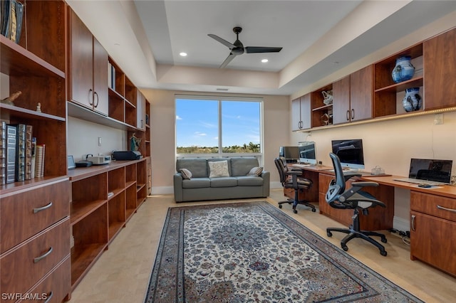 home office with ceiling fan, a raised ceiling, and built in desk