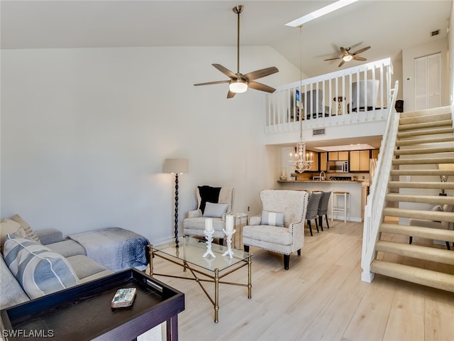 living room featuring high vaulted ceiling, ceiling fan with notable chandelier, and light wood-type flooring