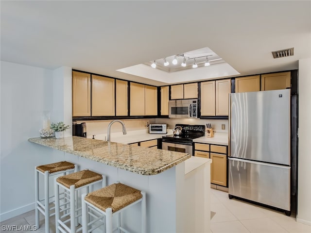 kitchen with kitchen peninsula, light stone countertops, stainless steel appliances, rail lighting, and a breakfast bar area